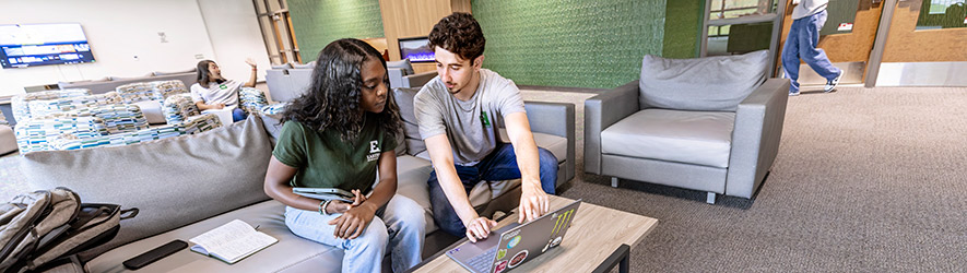 Two Eastern Michigan University students sit on a couch in a campus lounge, collaborating and looking at a laptop computer together.